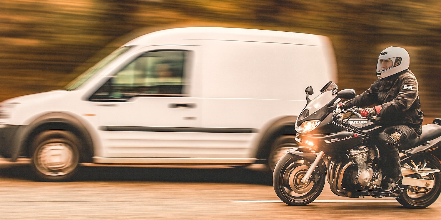 Fekete Suzuki motoros előz egy fehér pickup furgont.
