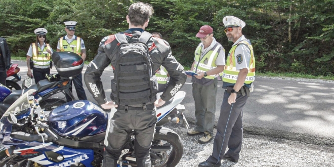 Rendőrök és egy műszaki ellenőr közúti ellenőrzésen vizsgál egy motort, a motoros háttal áll.